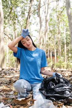 woman holds a garbage bag and a group of Asian volunteers clean up the area in the forest to preserve the natural ecosystem.