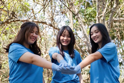 A group of Asian volunteers joined hands before helping to collect trash in plastic bags and clean areas in the forest