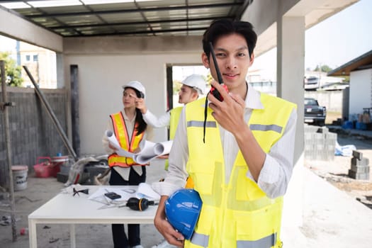 Portrait of a male engineer at a construction site using a walkie-talkie. Standing in charge of planning a construction project in formal attire, wearing a hard hat, a successful civil engineer..