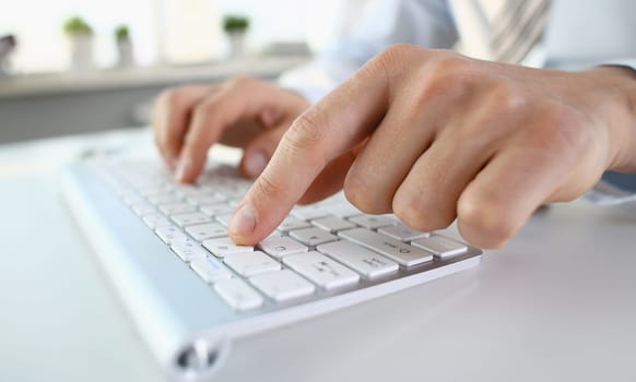 Male arms in suit typing on white keyboard using computer pc at office workplace closeup. Accountant finger job modern lifestyle web search assistant enter account login password and note credential