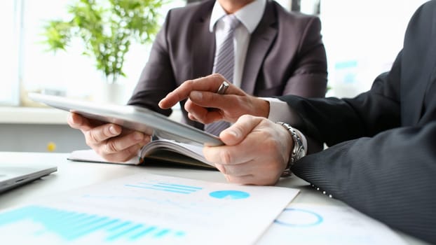 Two businessman are looking and studying statistics on tablet display closeup. Male hand opponent holds pen and points out problem collaboration business coach cooperation partnership palm concept