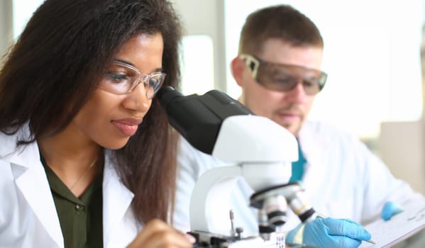 Two scientists of a student chemist are conducting research using microscope for bacterial contamination of water to search for vaccine to treat diseases in medicine