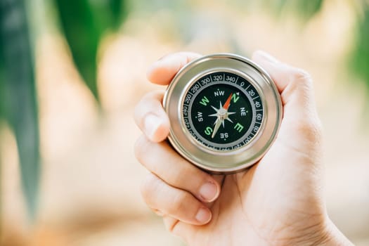 A traveler hand holds a compass in a park representing the search for direction and guidance. Amidst nature beauty the compass signifies exploration and discovery.