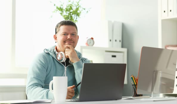 Handsome smiling male student using online education service. Young man looking in laptop display watching training course and listening it with headphones. Modern study technology concept