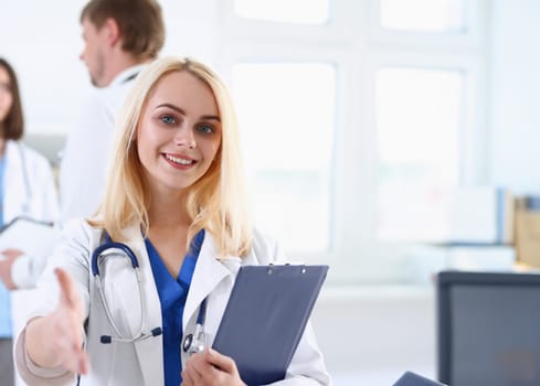 Female medicine doctor hold pad and give arm to shake in office closeup. Friend welcome introduction or thanks gesture test work examine patient congratulation help exam teamwork deal concept