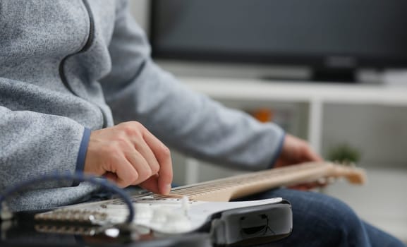 Male hands at home play and tune the electric guitar is engaged in music realizes listening enjoying music notation large concept closeup