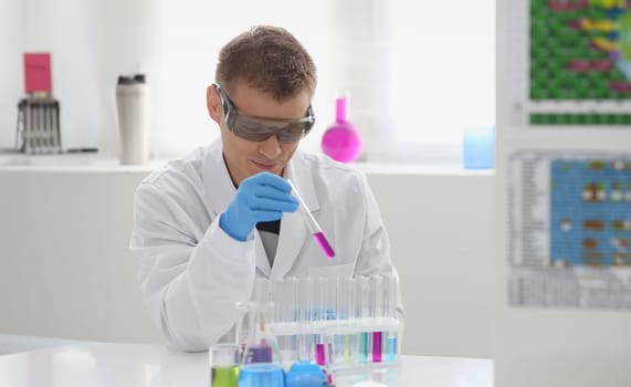 A male chemist holds test tube of glass in his hand overflows a liquid solution of potassium permanganate conducts an analysis reaction takes various versions of reagents using chemical manufacturing.