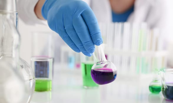 A male chemist holds test tube of glass in his hand overflows a liquid solution of potassium permanganate conducts an analysis reaction takes various versions of reagents using chemical manufacturing.