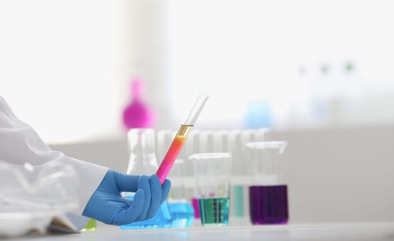 A male chemist holds test tube of glass in his hand overflows a liquid solution of potassium permanganate conducts an analysis reaction takes various versions of reagents using chemical manufacturing.