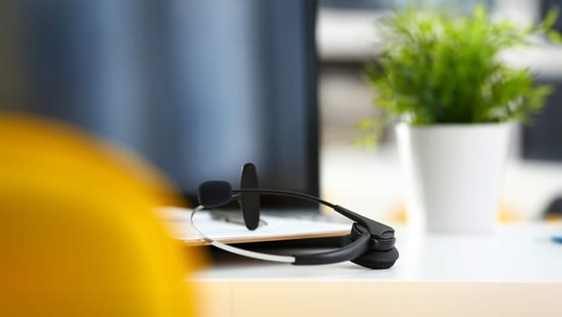 Empty remote office workplace with laptop pc and headset closeup. Receptionist or secretary of contact data center desktop keyboard device desk table ip telephony or callcenter voice message system