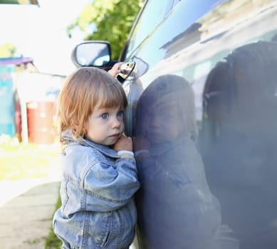 Little fashion child holds the car handle in a jeans jacket smiles and looks into the camera suitable for a fashion store