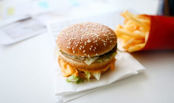 Hamburger and french fries with headphones lay on the desktop in the office during lunch break food delivery concept