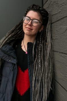 Street fashion concept, young European woman with dreadlocks wearing a dark jacket in an urban environment
