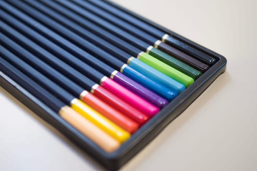 A variety of colored pencils are neatly arranged in a row on a table, resembling a colorful array of office supplies