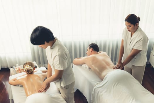 Caucasian couple customer enjoying relaxing anti-stress spa massage and pampering with beauty skin recreation leisure in day light ambient salon spa at luxury resort or hotel. Quiescent