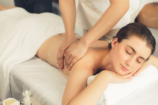 Caucasian couple customer enjoying relaxing anti-stress spa massage and pampering with beauty skin recreation leisure in day light ambient salon spa at luxury resort or hotel. Quiescent
