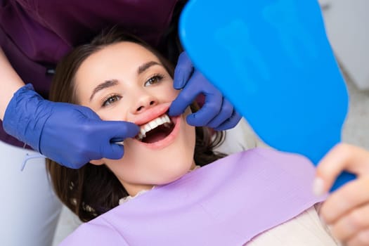 Dentist shows the results of dental treatment to patient, while woman looks in the mirror.