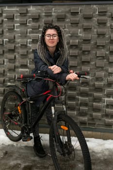 Urban charming woman with dreadlock hairstyle rides a bicycle in the cold season.