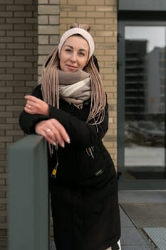 Well-groomed young woman dressed in a winter black coat with a scarf in an urban environment.
