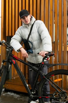 Young man in autumn clothes with a shoulder bag with a bicycle on the street.