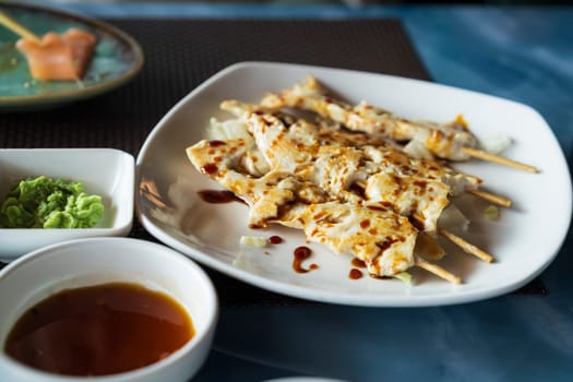 Teriyaki chicken skewers on plate on left soy sauce and wasabi sauce