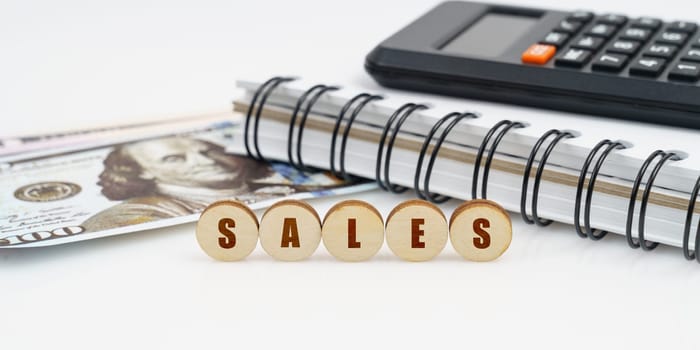 Business and finance concept. On a high surface lie a notepad, a calculator, dollars and wooden circles with the inscription - SALES