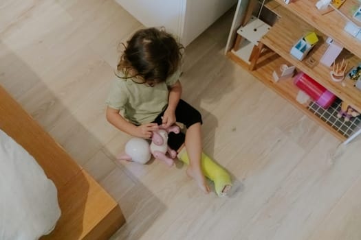 One Caucasian beautiful girl with a green headband sitting on the floor plays with a toy, early in the morning in her room, close-up top view.