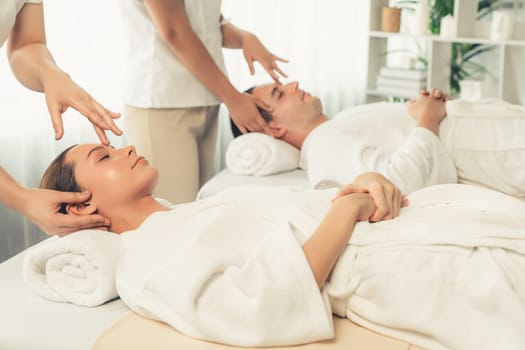 Caucasian couple enjoying relaxing anti-stress head massage and pampering facial beauty skin recreation leisure in dayspa modern light ambient at luxury resort or hotel spa salon. Quiescent