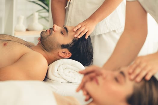 Caucasian couple enjoying relaxing anti-stress head massage and pampering facial beauty skin recreation leisure in dayspa modern light ambient at luxury resort or hotel spa salon. Quiescent