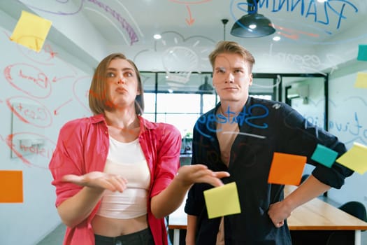 Couple of businesspeople discussing and brainstorming about solving marketing problem in front of glass board at business meeting by using mind map and sticky notes. Working together. Immaculate.