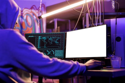 Man hacking online server on computer with empty screen mock up. Hacker in hood programming malicious software and cracking password while looking at white blank monitor at night