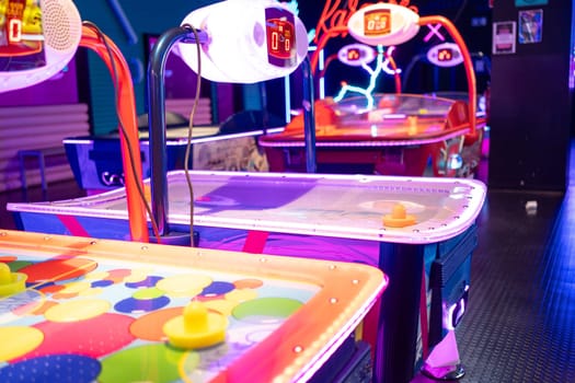 Neon Illuminated air hockey tables at illuminated children's entertainment center, accompanied by various gaming machines in an arcade.