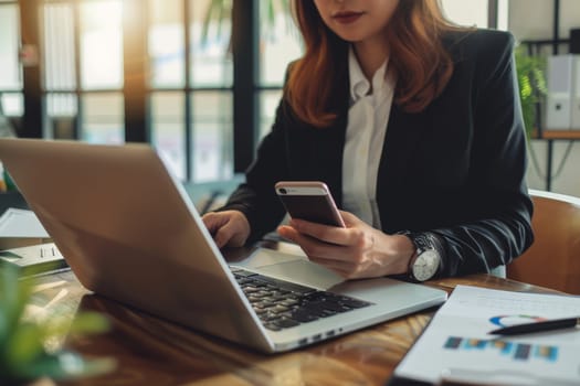 Close up of Businesswoman using smartphone while working on laptop.