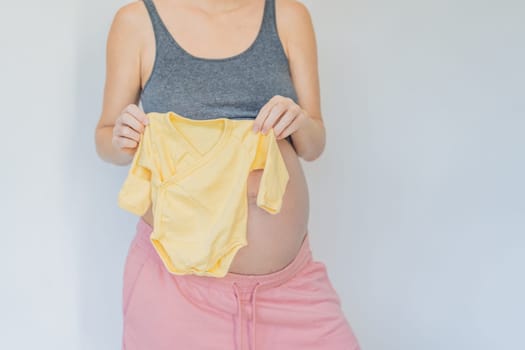 In a tender moment of anticipation, a pregnant woman cradles her unborn baby's clothes in her hands, savoring the sweetness of preparing for the little one's arrival.