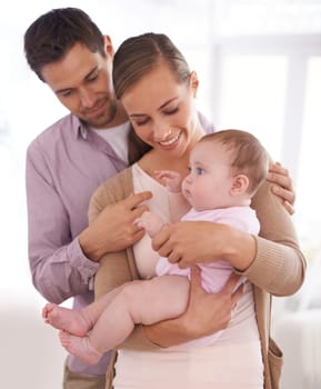 Mother, father and baby with happiness in home for healthy development, security and comfort in apartment. Family, man and woman with infant, smile and embrace for parenting, bonding or love in house.