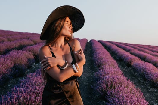 Close up portrait of young beautiful woman in a white dress and a hat is walking in the lavender field and smelling lavender bouquet.