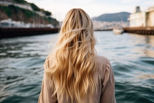 Rear view of a blonde girl on the shore of a stormy sea. Photo from the back of a woman looking over the horizon of the sea.