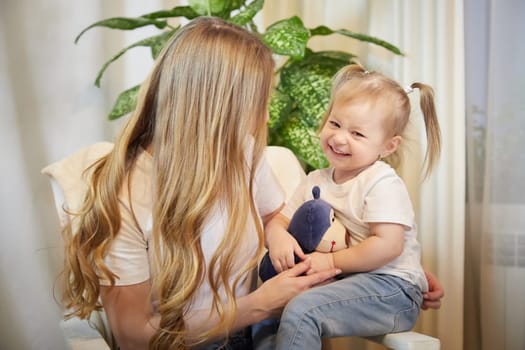 Happy loving family. Mother and daughter child girl playing and hugging in living room with wicker chair