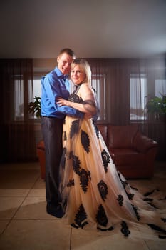 A plump woman in royal dress and a skinny man together in honeymoon hotel room. An adult newlywed couple embraces in an intimate setting. Queen Girl and guy in love