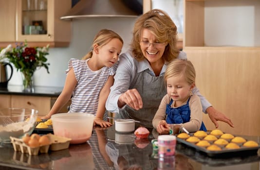 Grandma, kid and baking with teaching, smile and decorating for cheerful bonding together at home. Happy, pensioner or girl child with cupcake, laugh or icing for creative, playful or fun in kitchen.