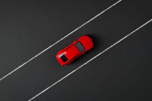 Top view of a red toy car driving on the drawn road line on a gray background