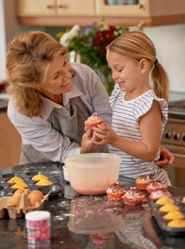 Grandmother, child and cupcake decorating in kitchen with icing or sprinkles or creativity, bonding or teamwork. Female person, girl and sweet treats or teaching with dessert ingredient, snack or fun.