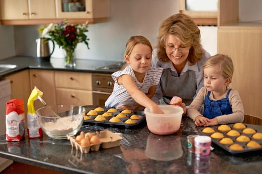 Grandmother, children and baking cupcakes or helping with icing decorations or learning creativity, bonding or teamwork. Woman, siblings and sweet treats or teaching with ingredients, snack or fun.