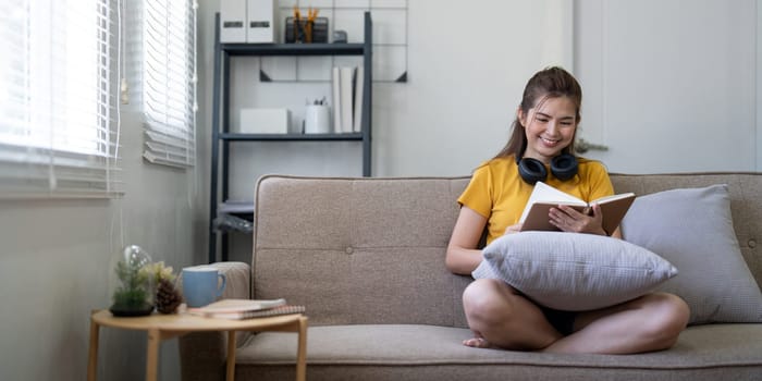 Young pretty woman siting on sofa and reading a book enjoys of rest. relaxing at home.