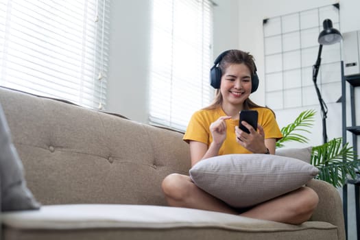 Young asian woman using mobile phone and earphones to listening to music or online chatting at home.