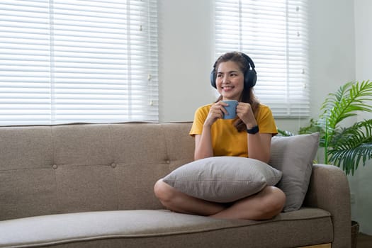 Young asian woman earphones to listening to music and drink coffee in the morning at home.