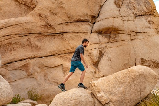 Young man on top of Joshua Tree rocks feeling free in the amazing landscape. . High quality photo