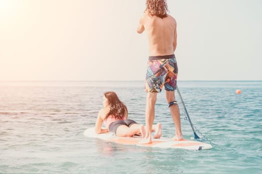 Sea woman and man on sup. Silhouette of happy young woman and man, surfing on SUP board, confident paddling through water surface. Idyllic sunset. Active lifestyle at sea or river