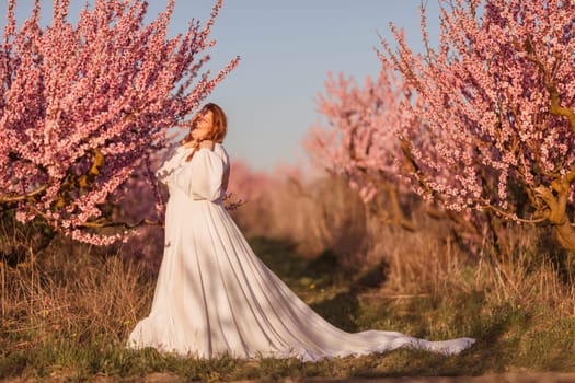 Woman blooming peach orchard. Against the backdrop of a picturesque peach orchard, a woman in a long white dress enjoys a peaceful walk in the park, surrounded by the beauty of nature