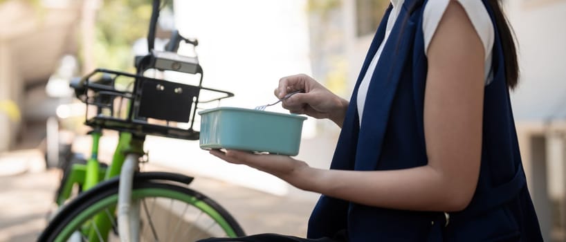 Young businesswoman while eating a lunch box sitting on a staircase during a break from work, concept healthy food using a bicycle for driving, Eco friendly vehicle, sustainable lifestyle concept.